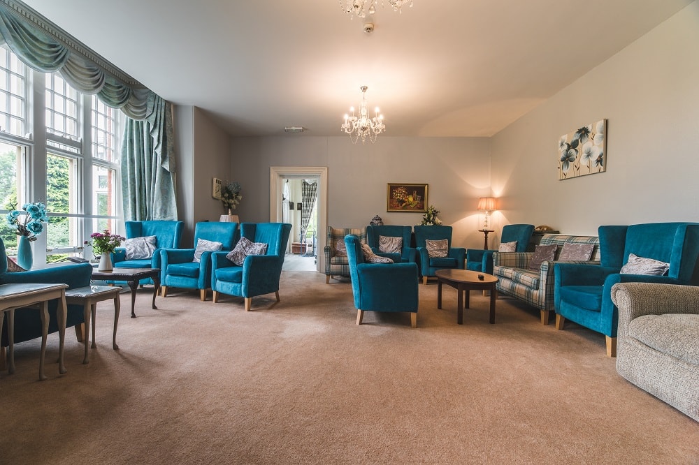 Living room with blue armchairs and sofas arranged neatly around wooden tables large windows with curtains and chandeliers
