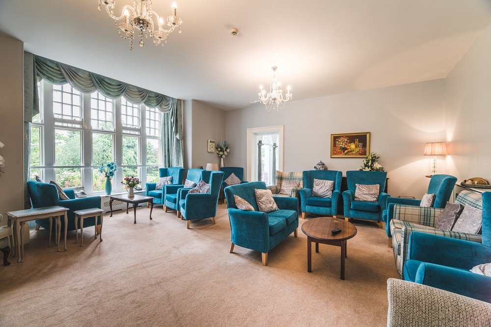 Living room with blue armchairs and sofas arranged neatly around wooden tables large windows with curtains and chandeliers