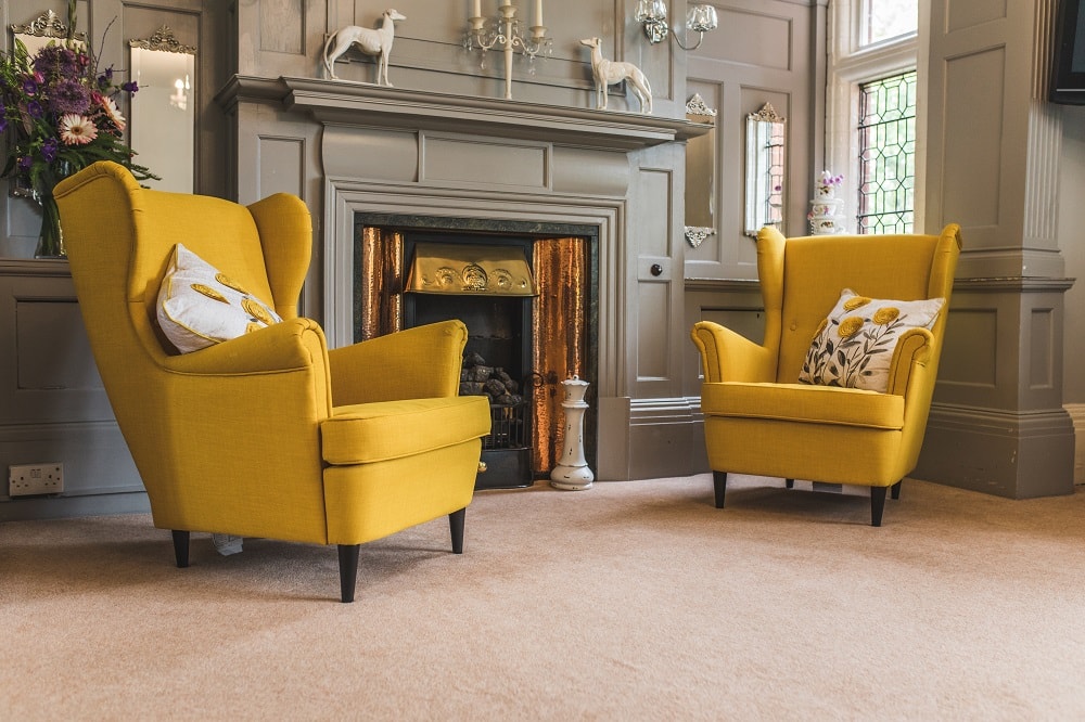 Living room with two bright yellow armchairs in front of a classic gray fireplace featuring decor including candle holders and decorative horse figures.