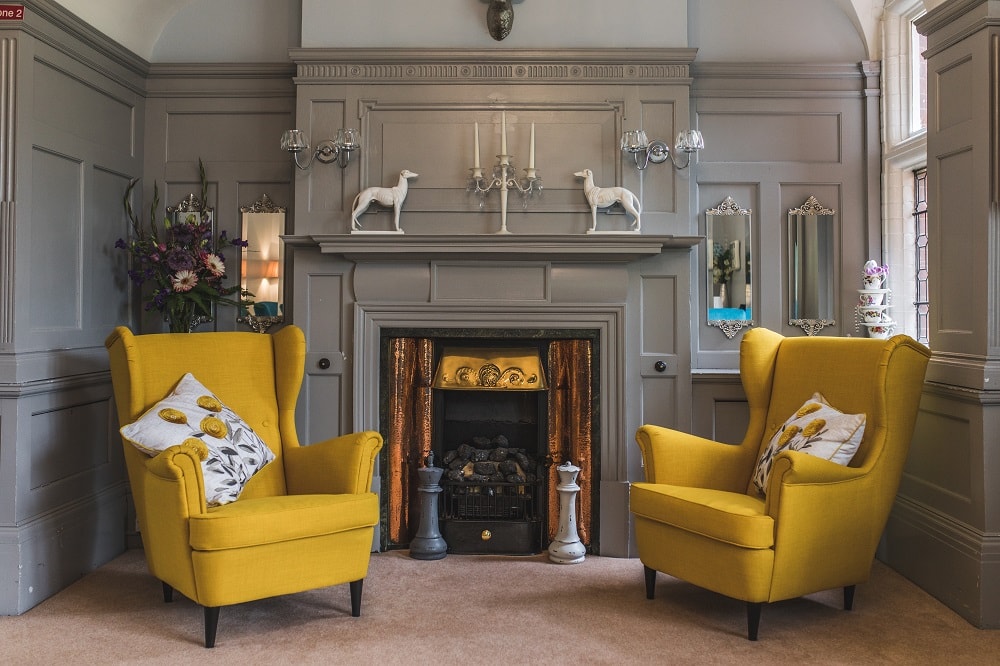 Living room with two bright yellow armchairs in front of a classic gray fireplace featuring decor including candle holders and decorative horse figures.