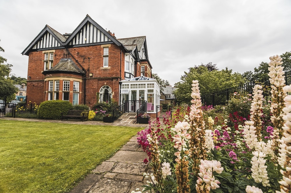 Red brick house with a lush garden and blooming flowers under a cloudy sky