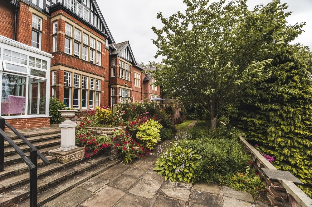 Exterior shot of care home brick building framed with large green shrubbery