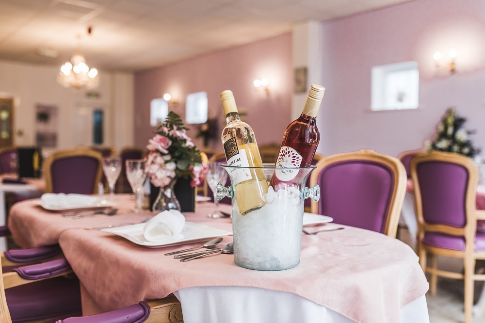 Set table featuring wine bottles in an ice bucket surrounded by purple chairs and soft lighting