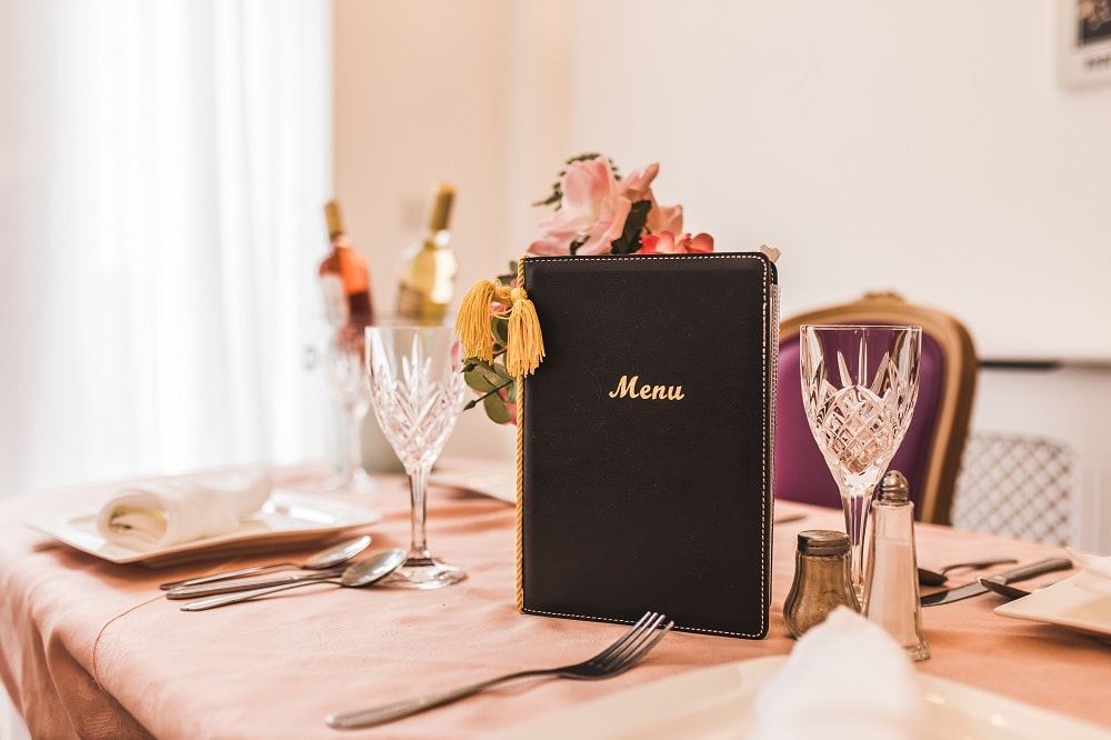 Table setting featuring a menu placed between crystal wine glasses, decorative napkins, and wine bottles