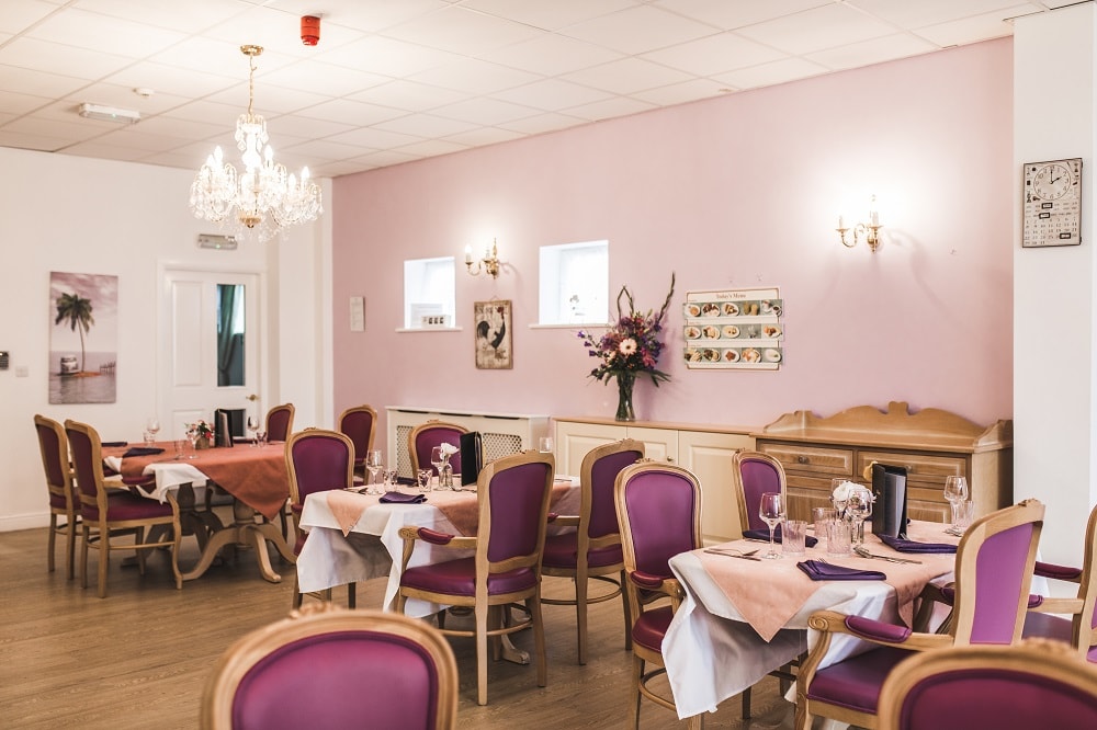 Dining room with tables covered in pink and white tablecloths set for guests