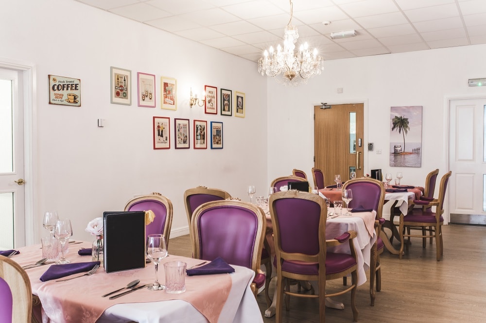 Dining area decorated with pink accents and purple chairs featuring large windows and soft lighting