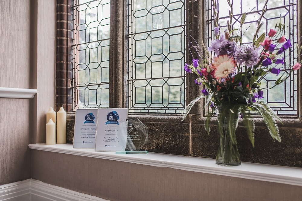 Award certificates and a glass plaque displayed on a windowsill next to candles in a well-lit room