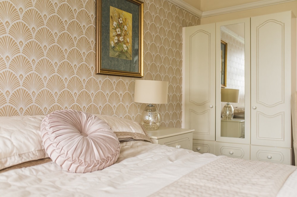 Bedroom interior with fan wallpaper, a plush bed with soft pillows, a wooden nightstand, a decorative lamp, and a matching mirrored wardrobe