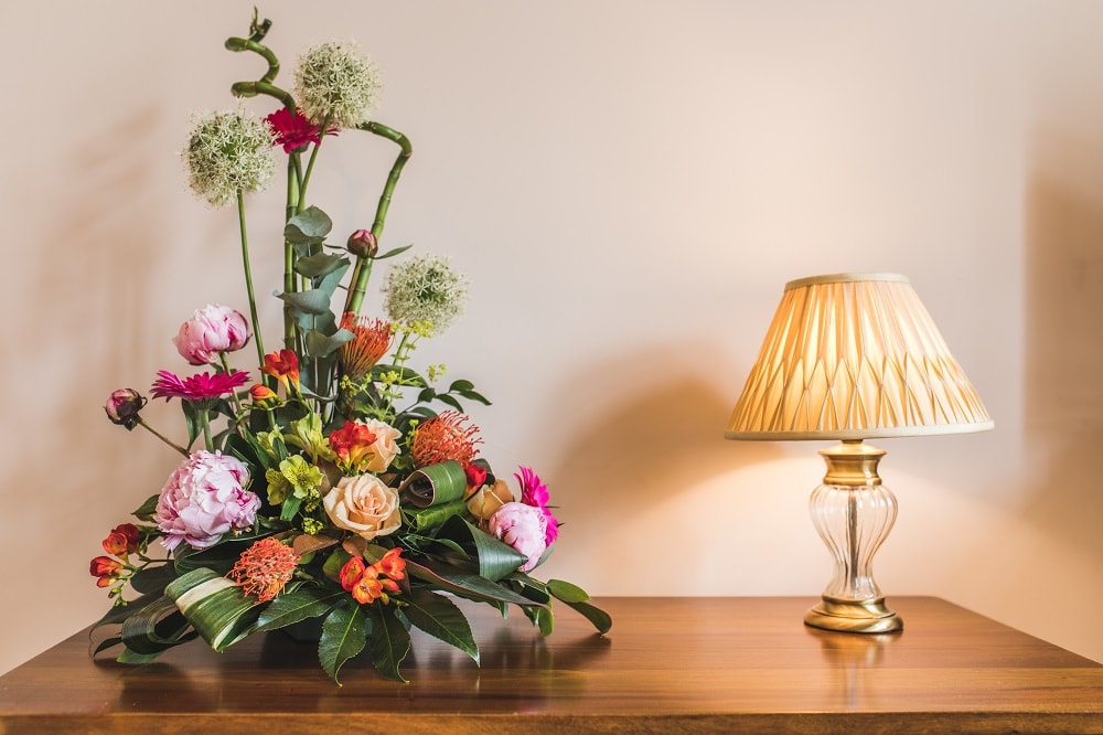 Floral arrangement with colorful blooms and lush greenery beside an elegant table lamp on a wooden surface
